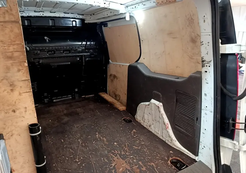 Vue intérieure arrière du fourgon Ford Transit blanc, montrant l'espace de chargement avec parois en bois et sol usé.
