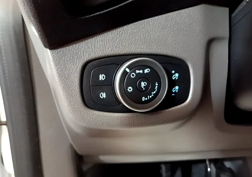 Gros plan sur le bouton de réglage des phares avec éclairage bleu, intérieur gris du Ford Transit Fourgon blanc.