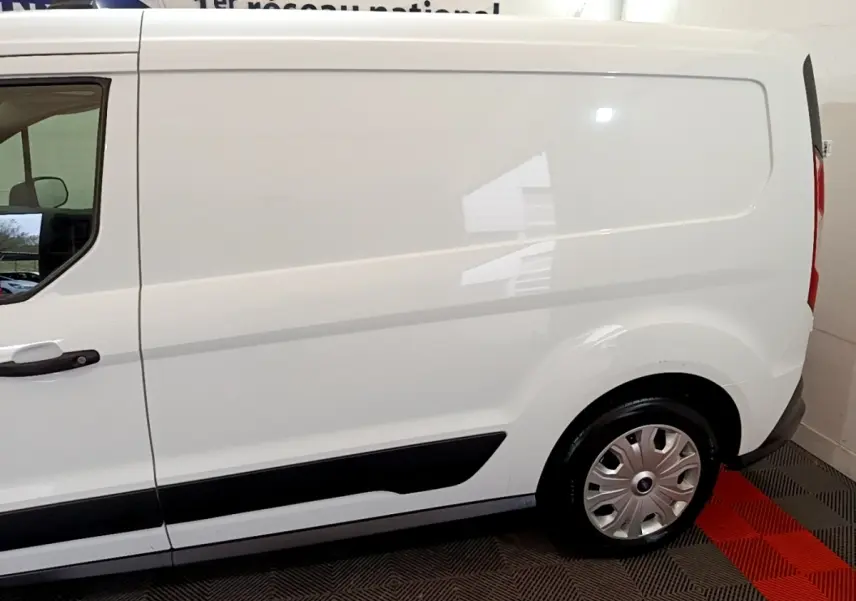 Vue latérale côté gauche d'un fourgon Ford Transit blanc, mettant en valeur la porte coulissante et la roue arrière.