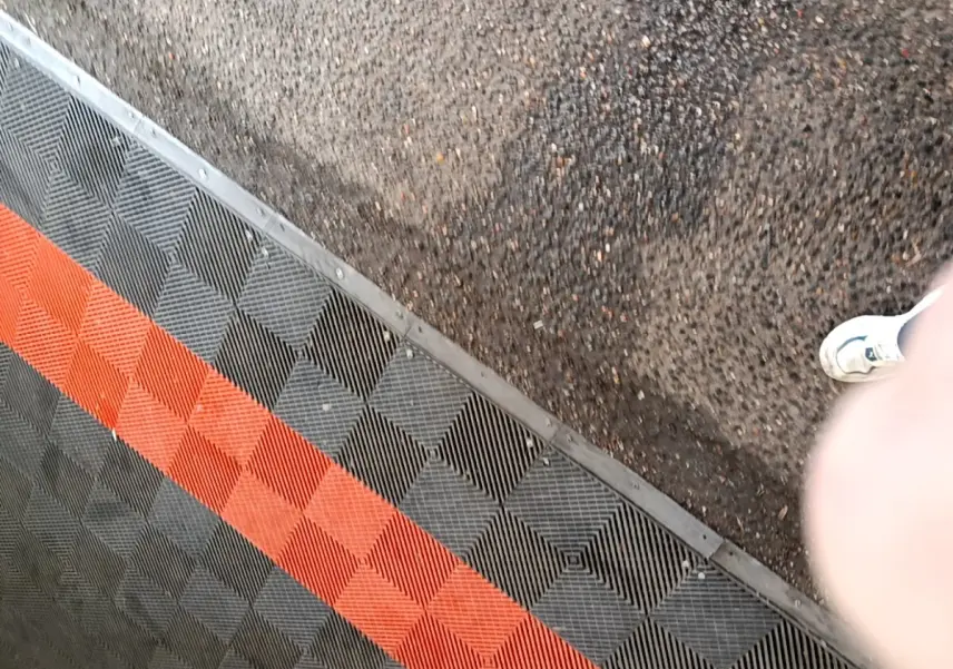 Vue partielle du sol avec un tapis en damier noir et rouge, sans véhicule visible.