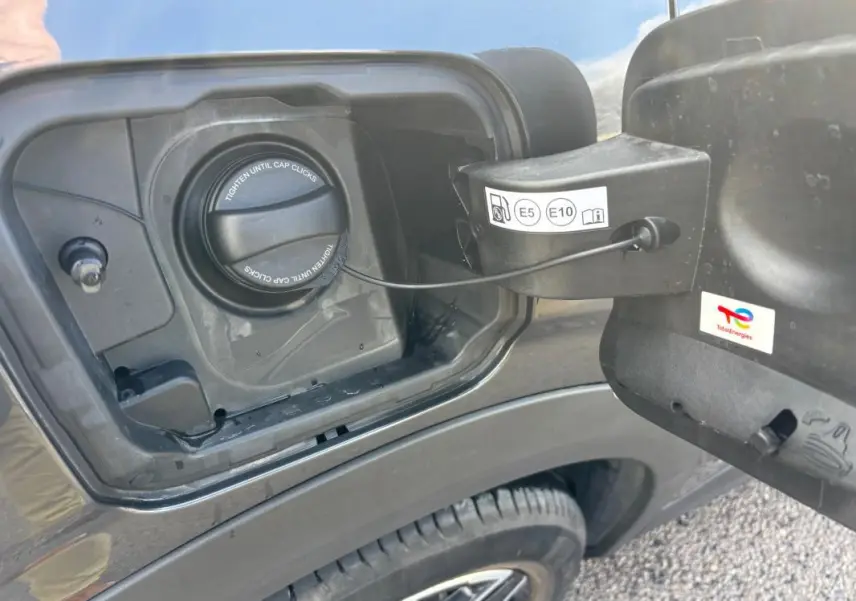 Gros plan sur la trappe à carburant côté gauche d’un Peugeot 3008 gris avec bouchon essence et jante alliage visible.