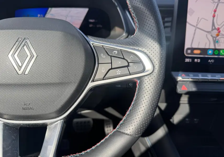 Gros plan sur le volant noir perforé du Renault Symbioz gris clair avec commandes intégrées et écran tactile visible.