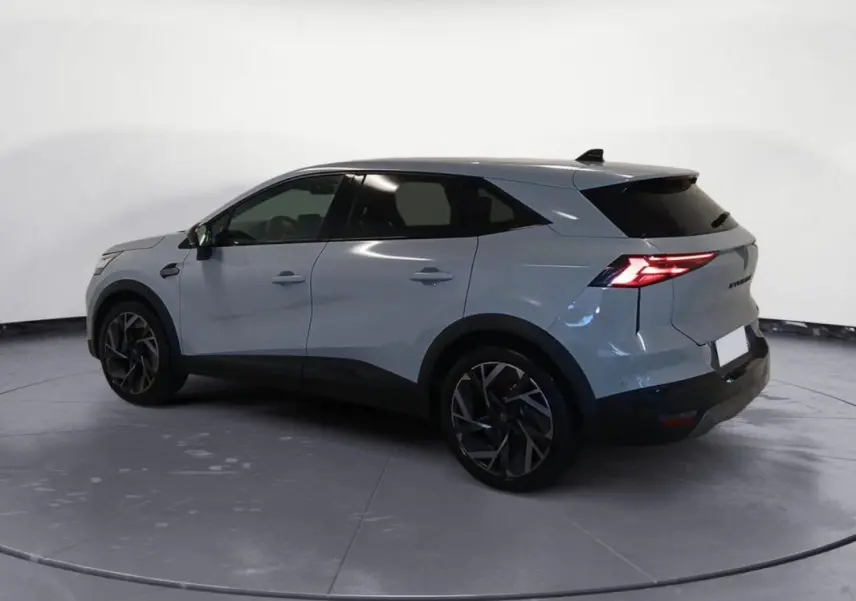 Renault Symbioz gris clair en vue 3/4 arrière droit, avec jantes alliage 19 pouces et feux arrière allumés.