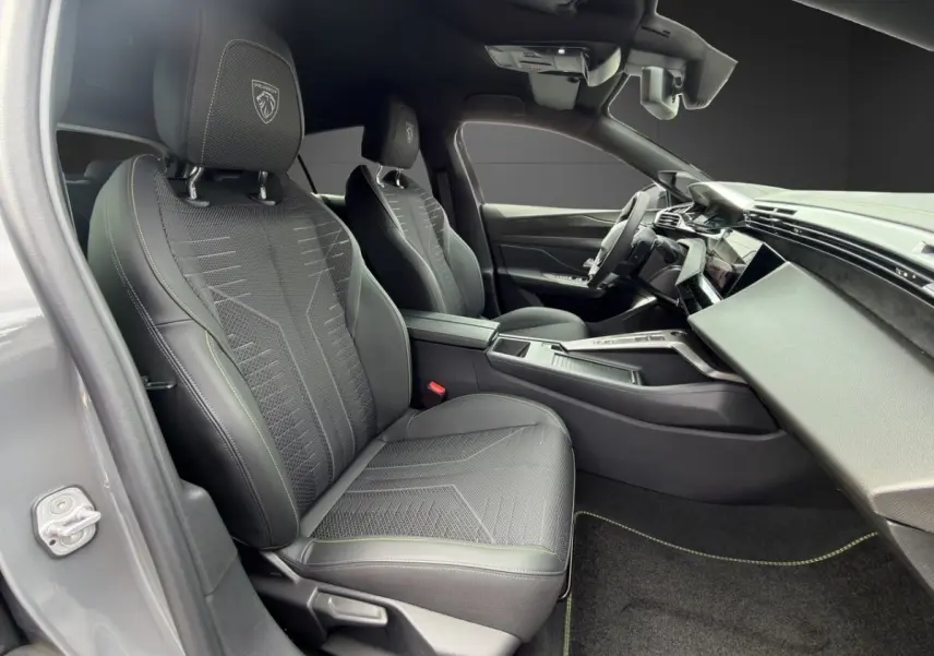 Vue intérieure côté conducteur de la Peugeot 308 gris clair 2026, sièges sport avec logo lion brodé et tableau de bord moderne.