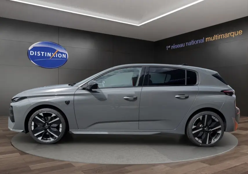 Vue de profil côté gauche d'une Peugeot 308 gris clair 2026 exposée en showroom avec jantes noires et grises distinctives.