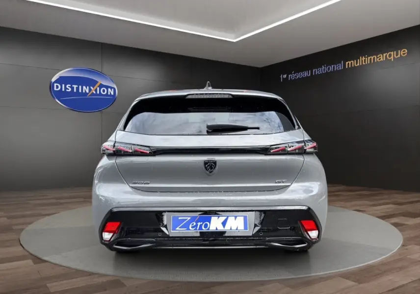 Vue arrière d'une Peugeot 308 GT gris clair avec feux arrière LED et logo noir brillant sur fond showroom.