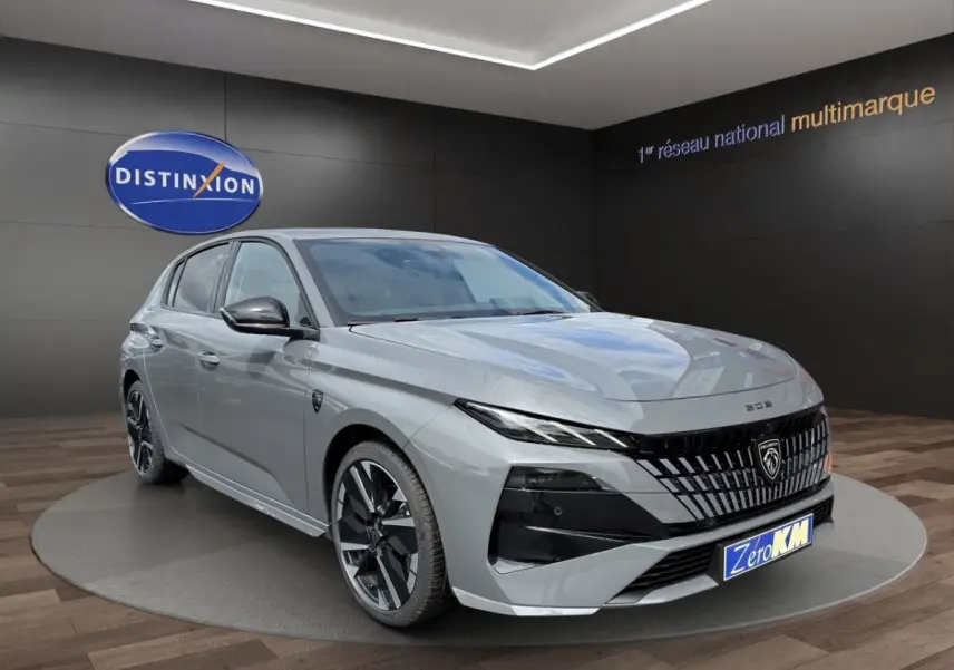 Peugeot 308 gris clair vue 3/4 avant droit, avec calandre noire distinctive et jantes noires brillantes.