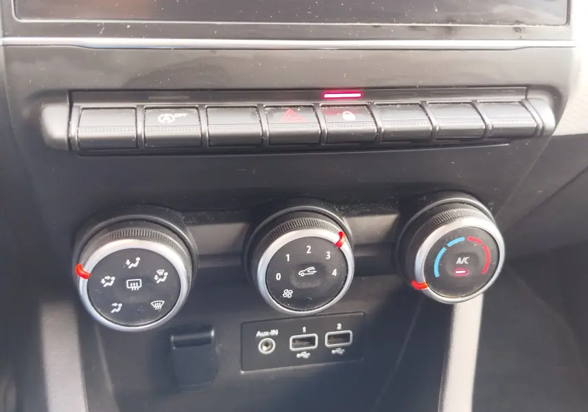 Gros plan sur les commandes de climatisation et ventilation de la Renault Clio bleu Iron, avec boutons rotatifs et ports USB visibles.