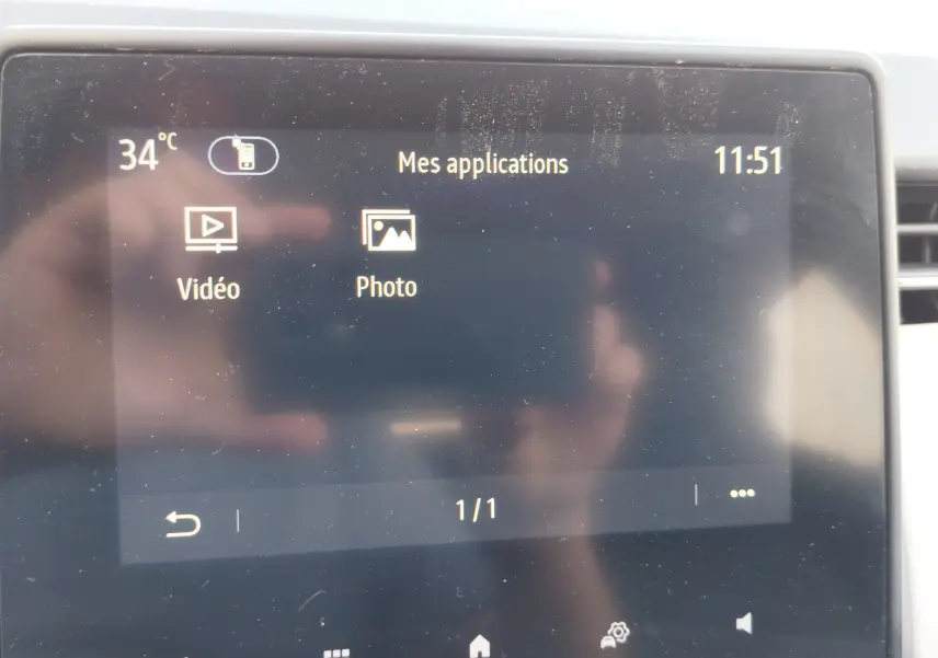 Écran tactile central de la Renault Clio 2022 affichant les applications vidéo et photo, avec reflet de main visible.