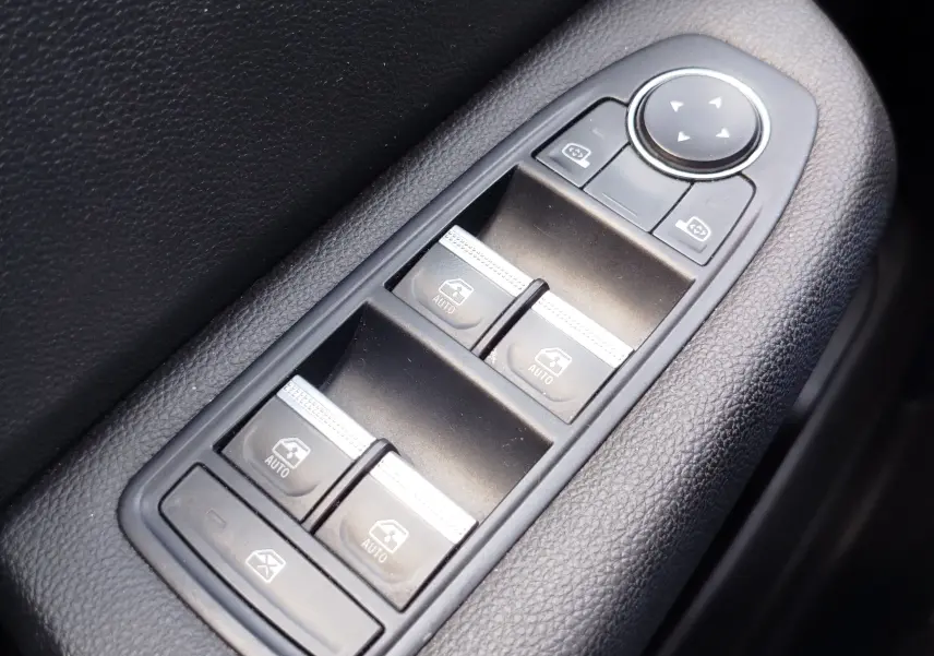 Gros plan sur les commandes de lève-vitres et rétroviseurs électriques en plastique noir à l'intérieur d'une Renault Clio Bleu Iron 2022.
