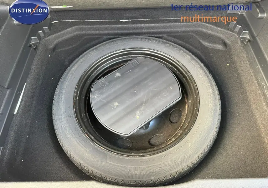 Pneu de secours noir logé dans le coffre d'un Citroën C5 Aircross blanc nacré, vue plongeante sur le rangement.