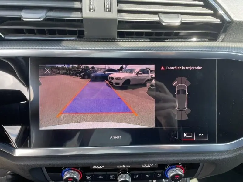 Vue de la caméra de recul sur l'écran du tableau de bord de l'Audi Q3 blanc, avec guidage de trajectoire visible.