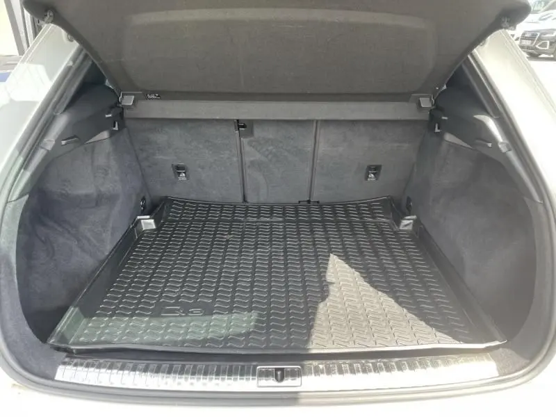 Coffre ouvert vu de l'arrière d'un Audi Q3 blanc 2021, avec tapis de protection noir et intérieur en tissu gris.