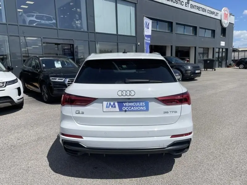Vue arrière d'un Audi Q3 blanc 35 TFSI 2021 avec badge S-Line et plaque "Véhicules Occasions" sur parking.