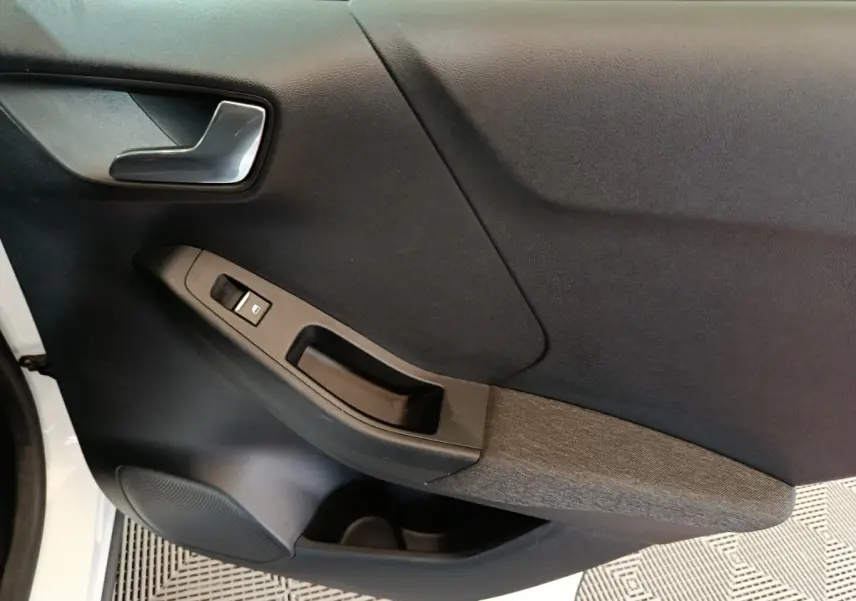 Vue rapprochée de la porte avant gauche noire avec poignée argentée et commande de lève-vitre sur Ford Puma blanc.