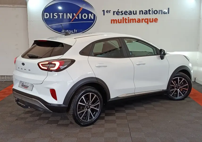 Vue 3/4 arrière droite d'un Ford Puma blanc 2022 avec feux arrière allumés et jantes noires en alliage.