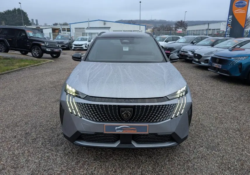 Vue avant d'un Peugeot 5008 gris métallisé 2025 avec calandre noire et feux LED en forme de griffes allumés.