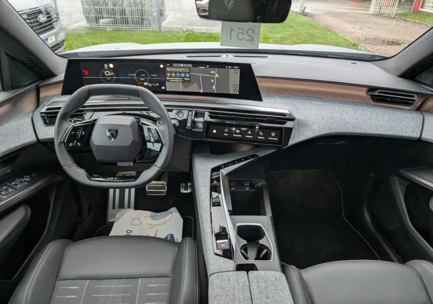 Vue intérieure avant du Peugeot 5008 gris 2025, tableau de bord moderne avec écran panoramique et volant compact noir.
