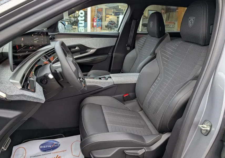 Vue intérieure côté conducteur du Peugeot 5008 gris 2025, sièges tissu et cuir avec logo Peugeot brodé sur appuie-tête.