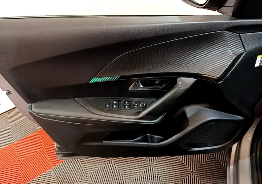 Vue intérieure côté gauche de la porte avant d’un Peugeot 2008 gris clair, avec commandes électriques et décor carbone.