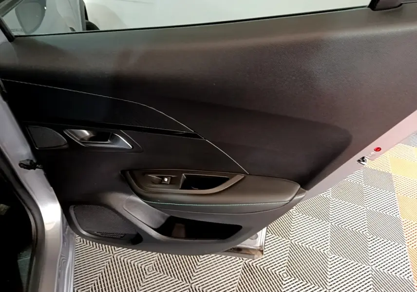 Vue intérieure côté gauche de la porte avant gris clair du Peugeot 2008 avec commandes de vitre et habillage noir.