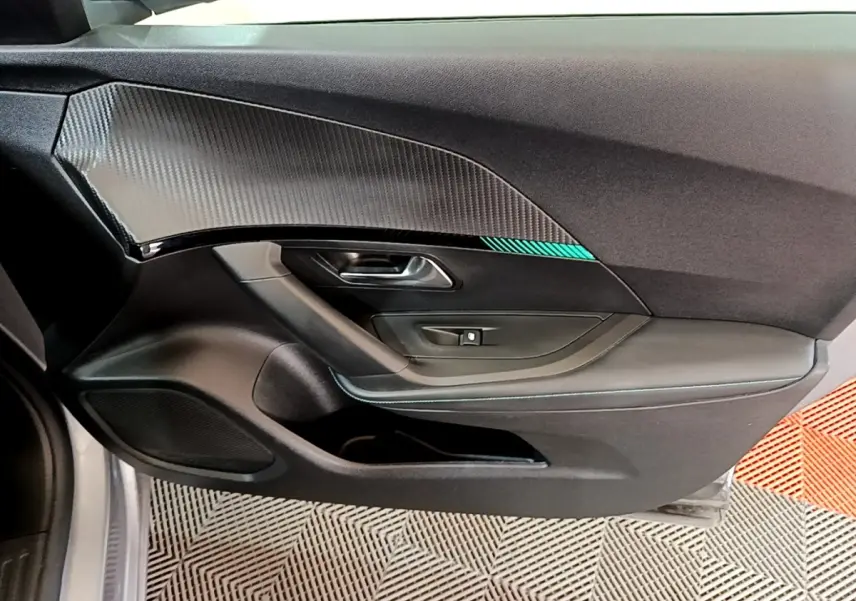 Vue intérieure côté gauche de la porte avant gris clair du Peugeot 2008 avec insert effet carbone et bouton de lève-vitre.