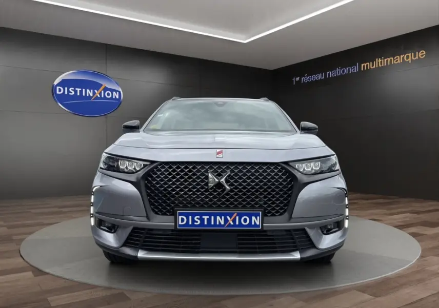 Vue frontale d’un DS7 Crossback gris clair avec calandre noire et feux LED, en showroom Distinxion.