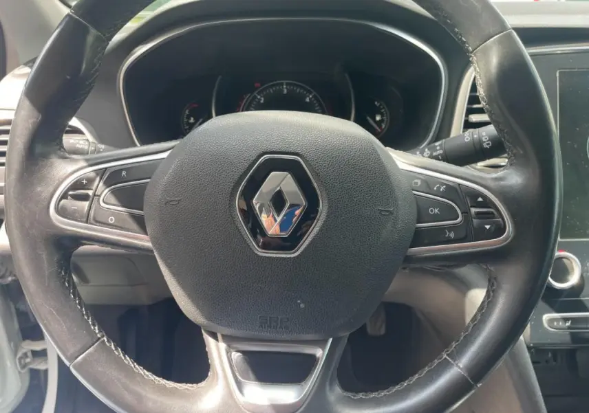 Vue rapprochée du volant noir de la Renault Mégane IV 2016 avec commandes intégrées et logo central chromé.