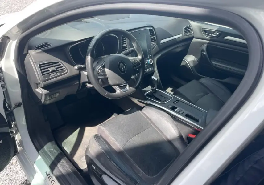 Vue intérieure côté conducteur de la Renault Mégane IV blanche de 2016, avec tableau de bord et console centrale visibles.