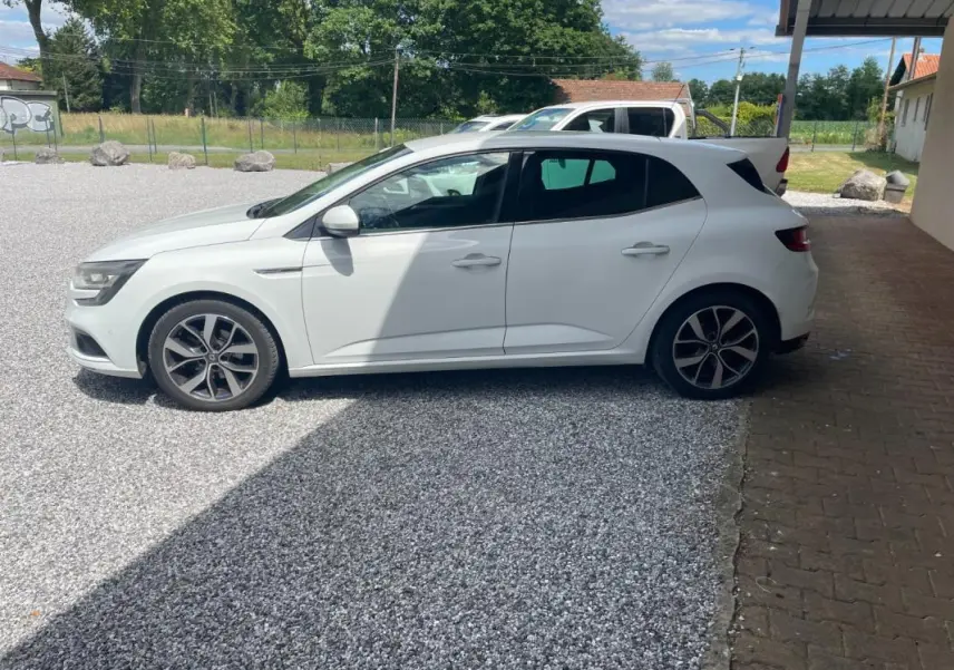 Renault Mégane IV blanche vue de profil côté gauche, garée sur gravier avec jantes alliage noires et grises.