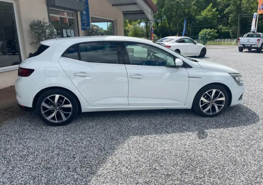 Renault Mégane IV blanche vue de profil côté gauche, avec jantes alliage distinctives et vitres teintées.