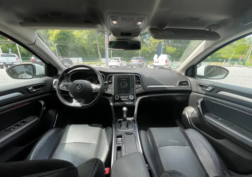 Vue intérieure avant de la Renault Mégane IV blanche de 2016, montrant le tableau de bord et les sièges en cuir noir.