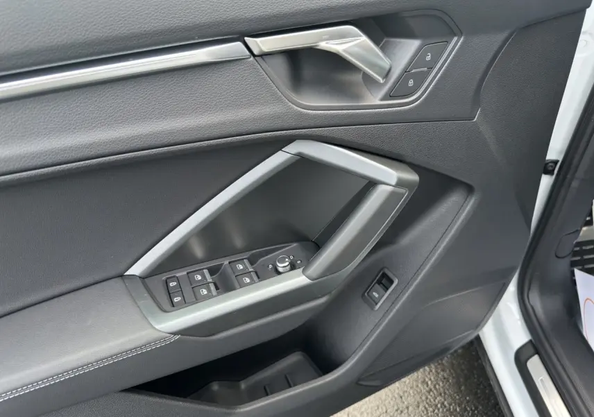 Détail de la porte avant droite de l'Audi Q3 Sportback blanc, avec commandes électriques et poignée grise.