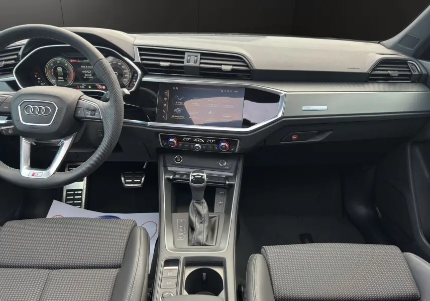 Vue intérieure avant de l'Audi Q3 Sportback S line 2024 avec tableau de bord noir et console centrale moderne.