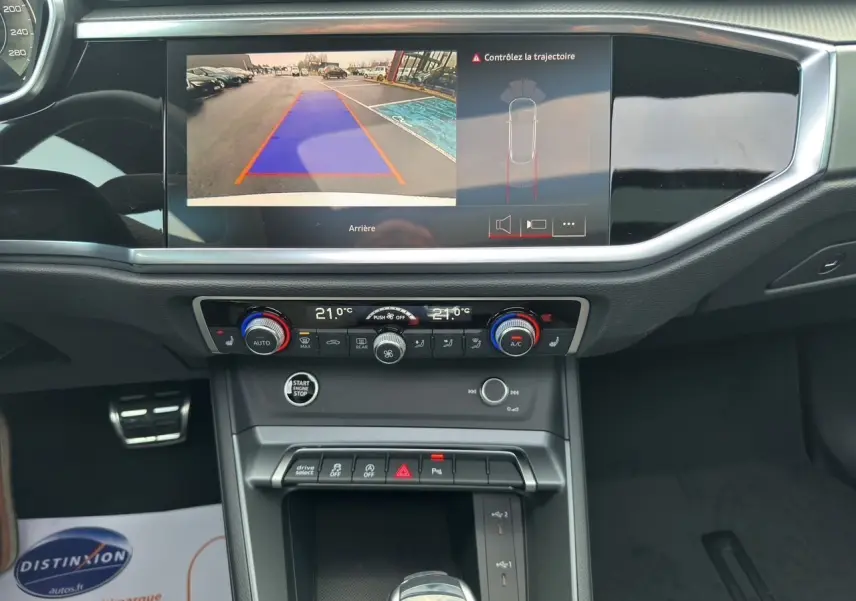 Intérieur de l'Audi Q3 Sportback blanc 2024, vue sur la console centrale avec écran caméra de recul et commandes climatisation.