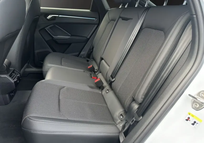 Vue côté droit des sièges arrière noirs en tissu et cuir de l'Audi Q3 Sportback blanc 2024 avec ceintures et porte ouvert.