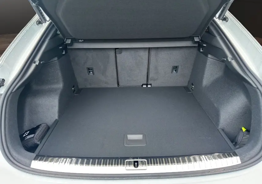 Coffre ouvert d'un Audi Q3 Sportback blanc, montrant un espace de chargement propre et bien fini avec tapis noir.