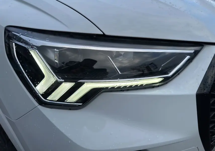Gros plan sur le phare avant droit LED d'un Audi Q3 Sportback blanc glacier avec éclairage distinctif en forme de flèche.