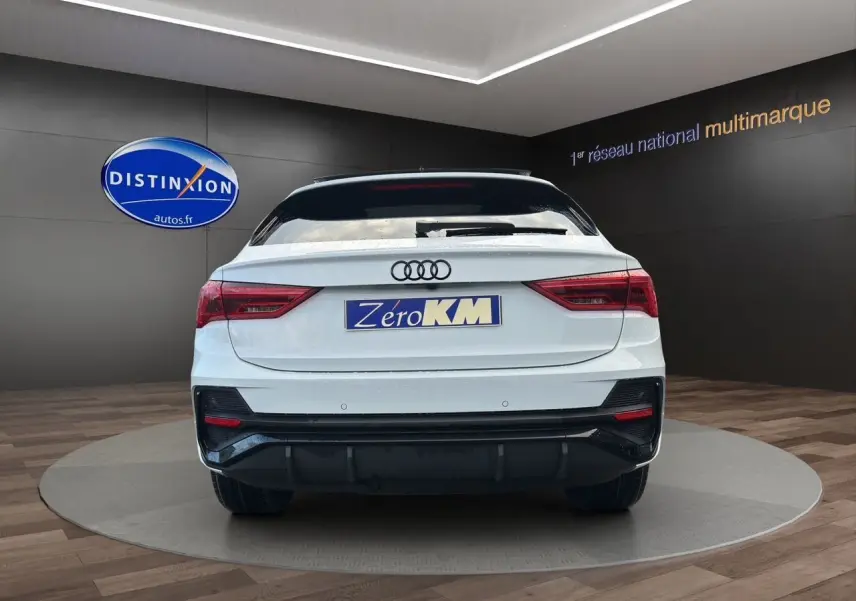 Vue arrière d'un Audi Q3 Sportback blanc Glacier avec pare-chocs S line et feux arrière LED dans un showroom