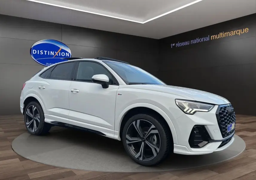 Audi Q3 Sportback blanc en 3/4 avant droit, avec jantes noires brillantes et toit panoramique visible.