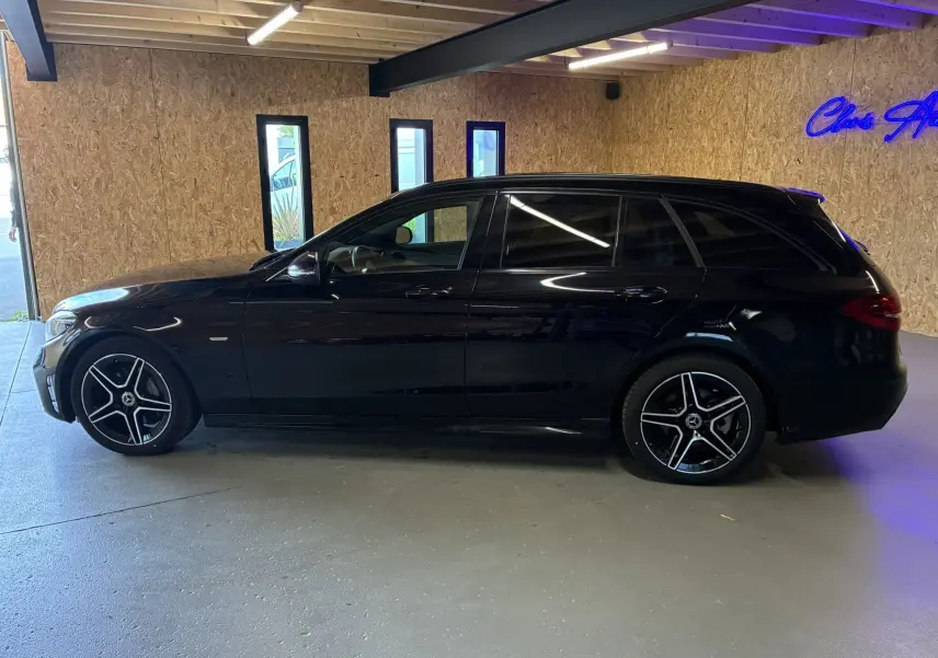 Profil droit d'un break Mercedes Classe C 220D AMG Line noir métal avec jantes alu bi-ton dans un garage.