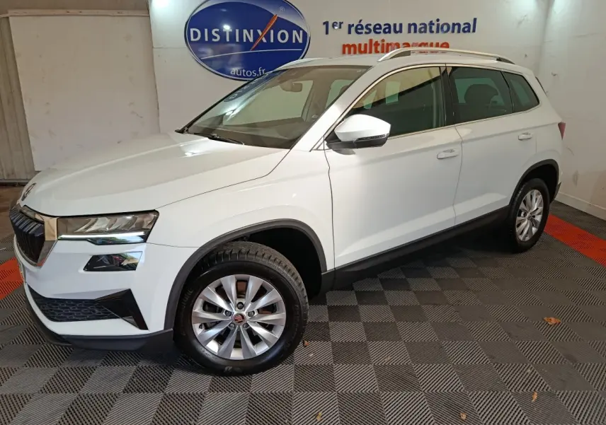 Vue 3/4 avant droite d’un Skoda Karoq blanc 2024, avec jantes alliage et rétroviseurs blancs, en intérieur showroom.