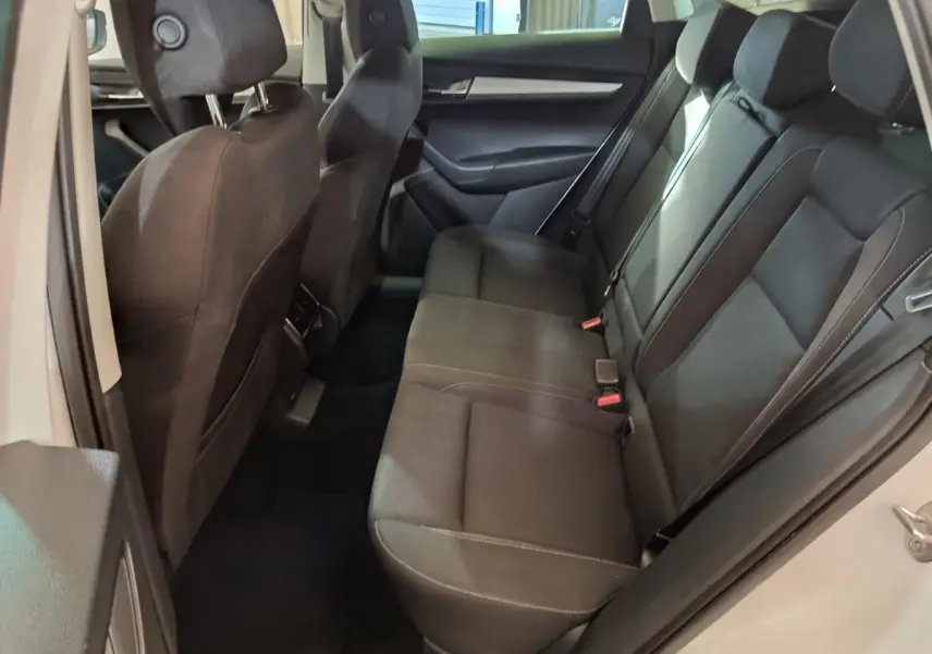 Vue latérale droite de l'intérieur arrière du Skoda Karoq blanc 2024 avec sièges noirs et ceintures visibles.