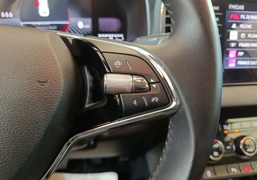 Gros plan sur les commandes gauche du volant cuir du Skoda Karoq 2024, avec tableau de bord et écran tactile en arrière-plan.