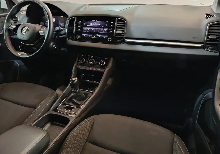 Vue intérieure avant du Skoda Karoq 2024, tableau de bord noir avec écran tactile central et volant cuir multifonctions.