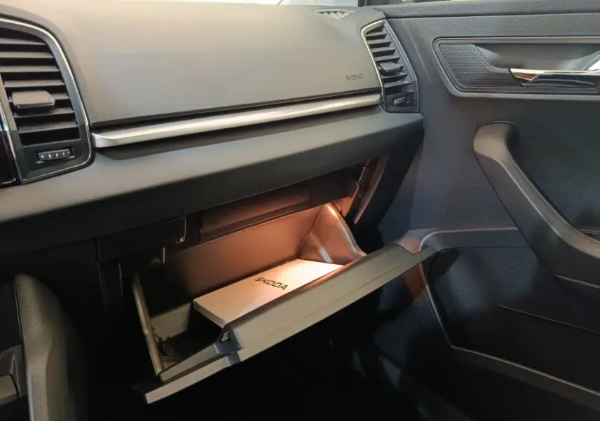 Intérieur noir de la Skoda Karoq 2024, vue côté passager avec boîte à gants ouverte et manuel Skoda visible.