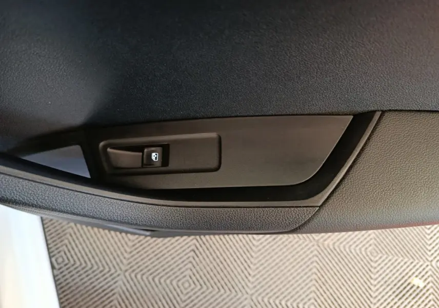 Gros plan sur le bouton de commande de la vitre électrique sur la porte intérieure noire d'un Skoda Karoq blanc.