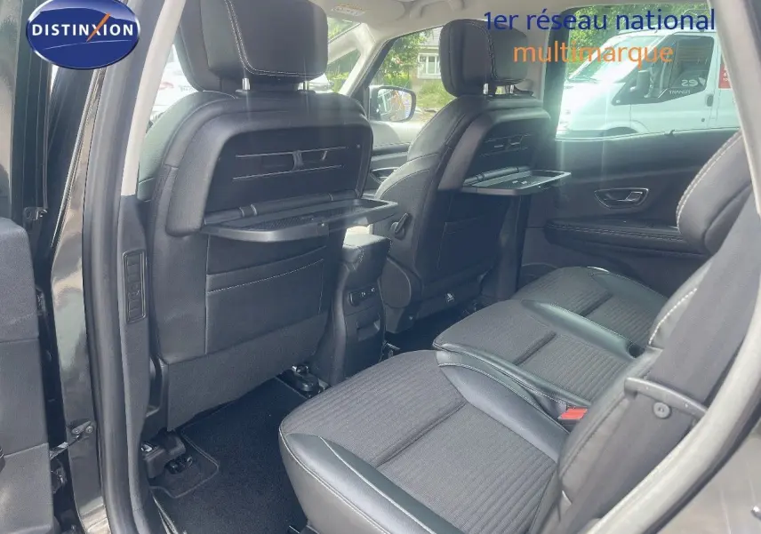 Vue intérieure arrière du Renault Scénic IV noir, montrant les sièges en tissu avec tablettes rabattables intégrées aux dossiers avant.