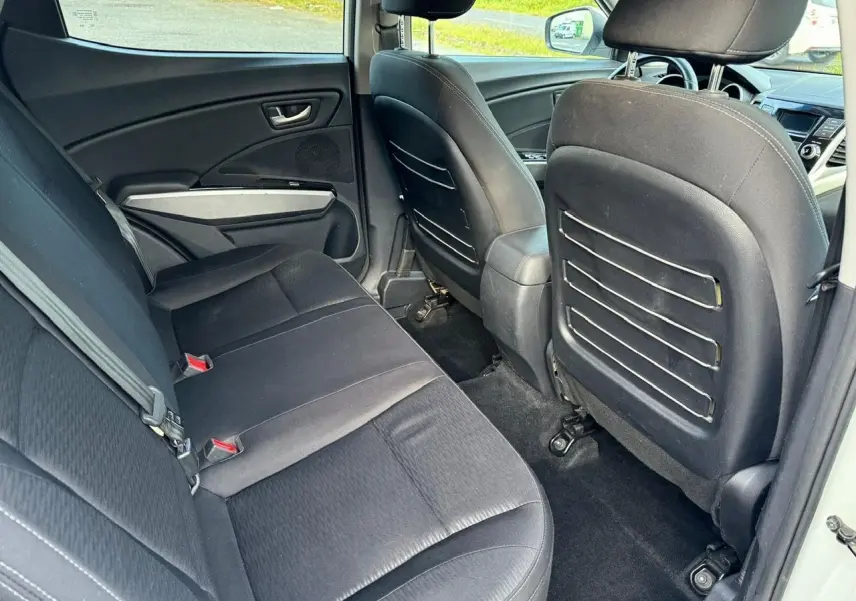 Vue intérieure arrière côté gauche du SSANGYONG TIVOLI blanc 2016, sièges noirs et rangements au dos des sièges avant.