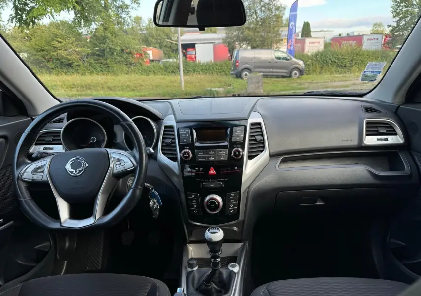 Intérieur du SsangYong Tivoli blanc 2016, vue frontale du tableau de bord avec volant et levier de vitesse manuel.